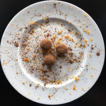 orange chocolate avocado truffles on a white plate with cocoa powder and orange zest sprinkled on truffles and plate