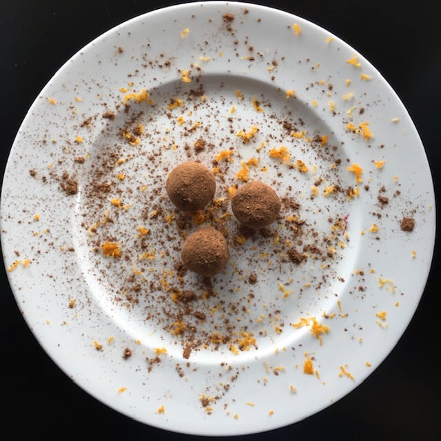 orange chocolate avocado truffles on a white plate with cocoa powder and orange zest sprinkled on truffles and plate