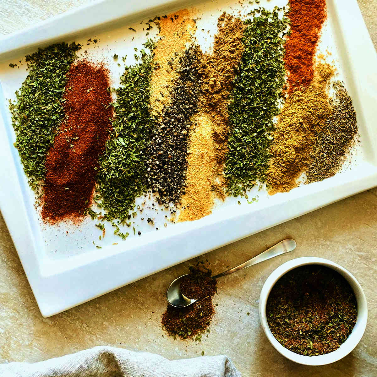 Tempero baiano brazilian spices layered next to each other on a white plate next to a dish of mixed seasoning and a spoonful