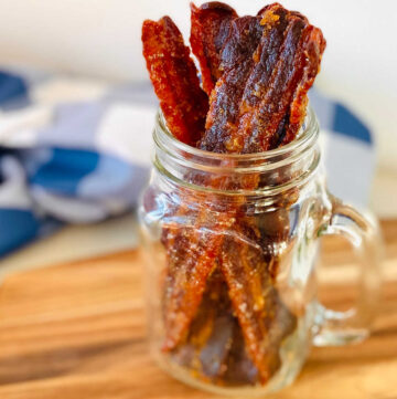 bacon jerky sitting upright in glass jar with blue napkin in background