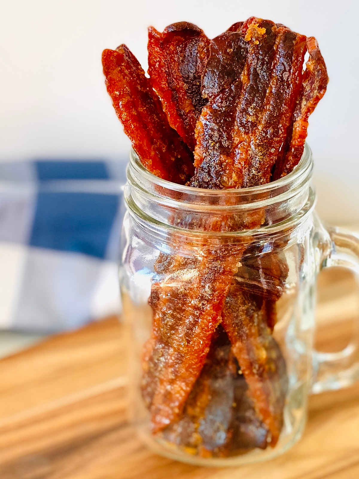 candied bacon jerky sitting upright in glass jar with blue napkin in background