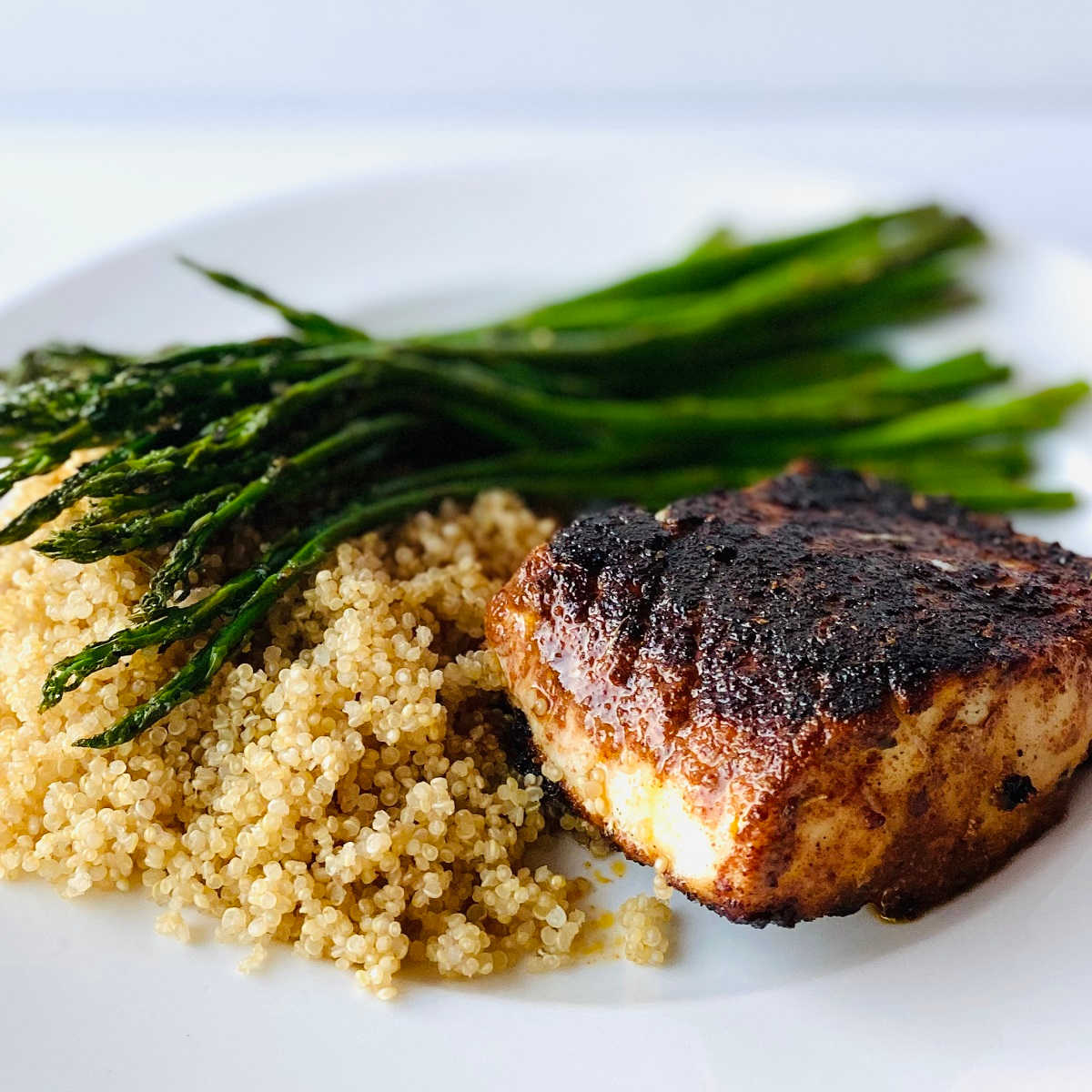 blackened cod on a plate next to quinoa and roasted asparagus