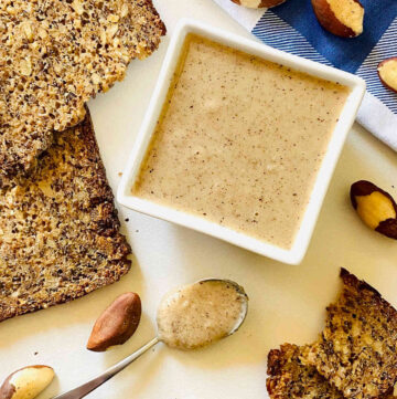 brazil nut butter in white dish next to bread, spoon and napkin