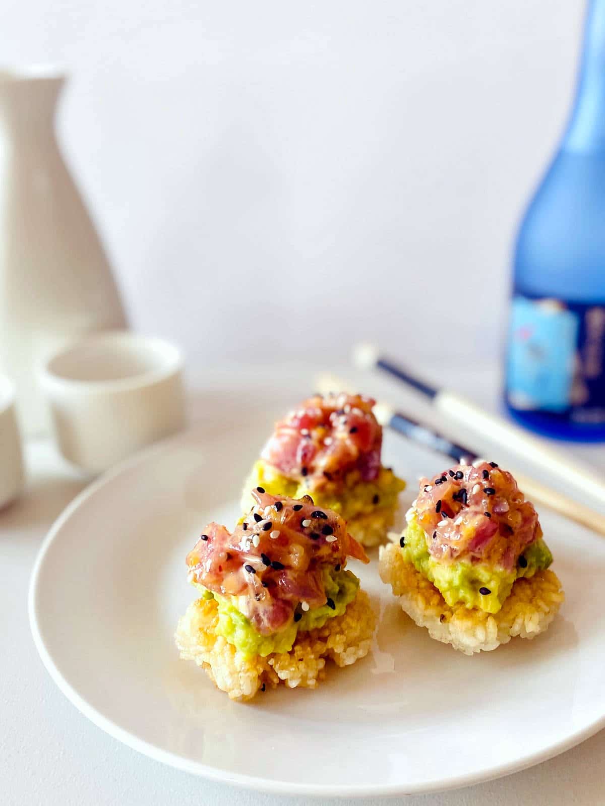 spicy tuna crispy rice on plate next to chopsticks, sake and sake carafe and glasses