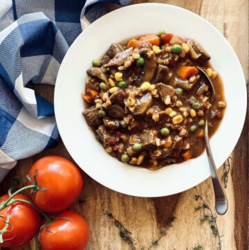 instant pot vegetable beef soup in white bowl with spoon next to napkin, tomatoes and herbs