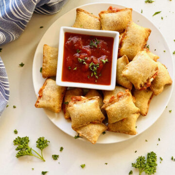 Air fryer pizza rolls on plate next to dish of marinara dipping sauce