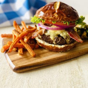 wagyu beef burger on cutting board next to sweet potato fries
