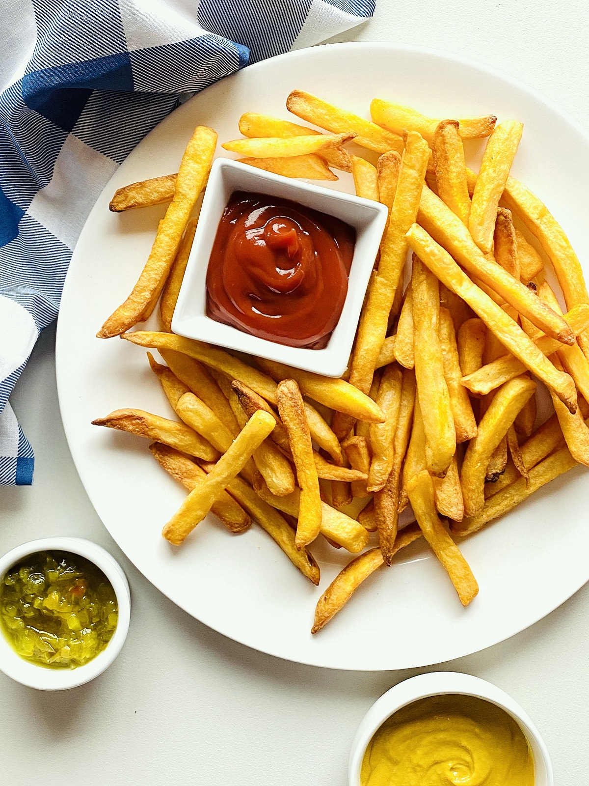 air fryer frozen french fries on a plate next to a dish of ketchup, relish and a blue napkin