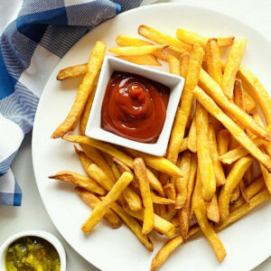 air fryer frozen french fries on a plate next to a dish of ketchup, relish and a blue napkin