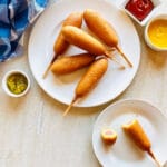 frozen air fryer corn dogs on a plate next to ketchup, mustard and relish