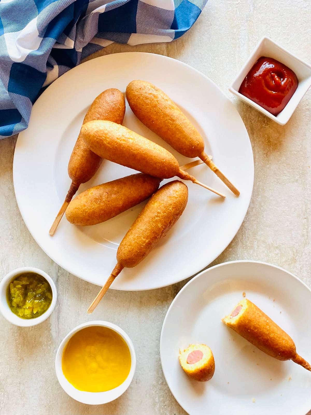 air fryer corn dogs on a plate next to ketchup, mustard and relish