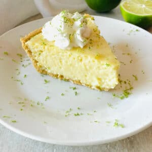 gluten free key lime pie on a plate next to limes topped with whipped cream and lime zest