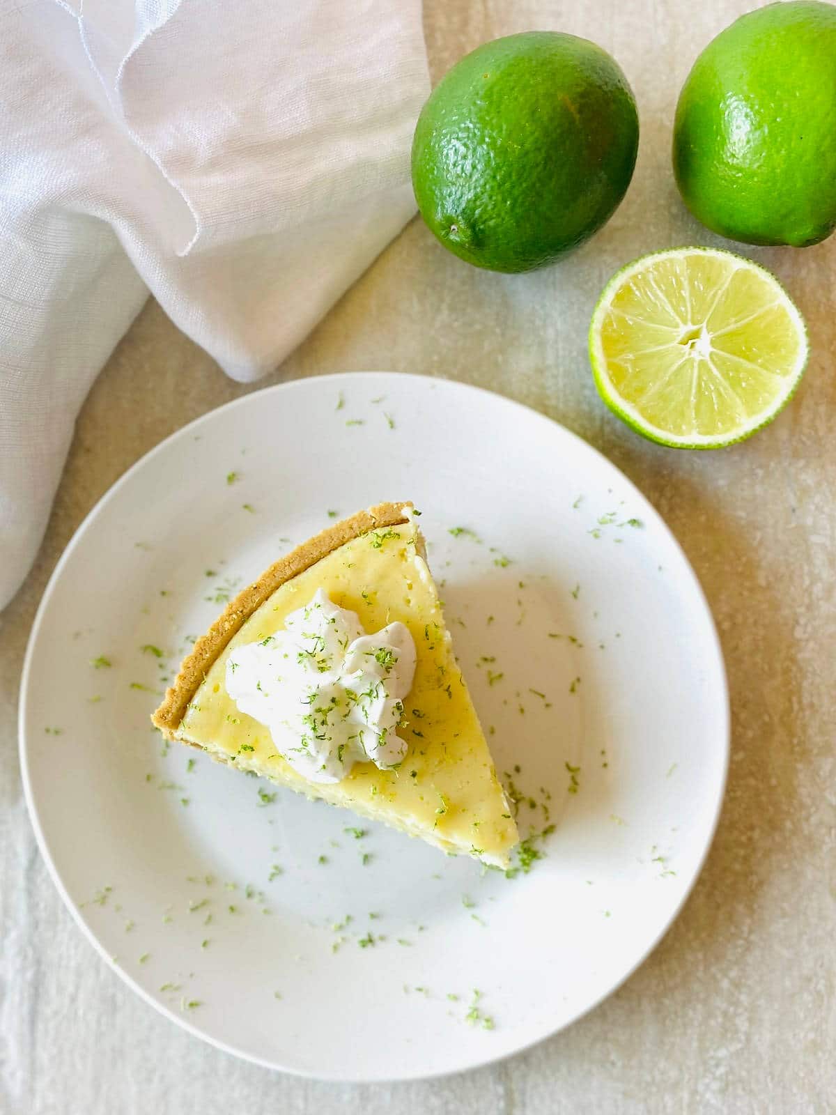 gluten free key lime pie on a plate next to limes topped with whipped cream and lime zest