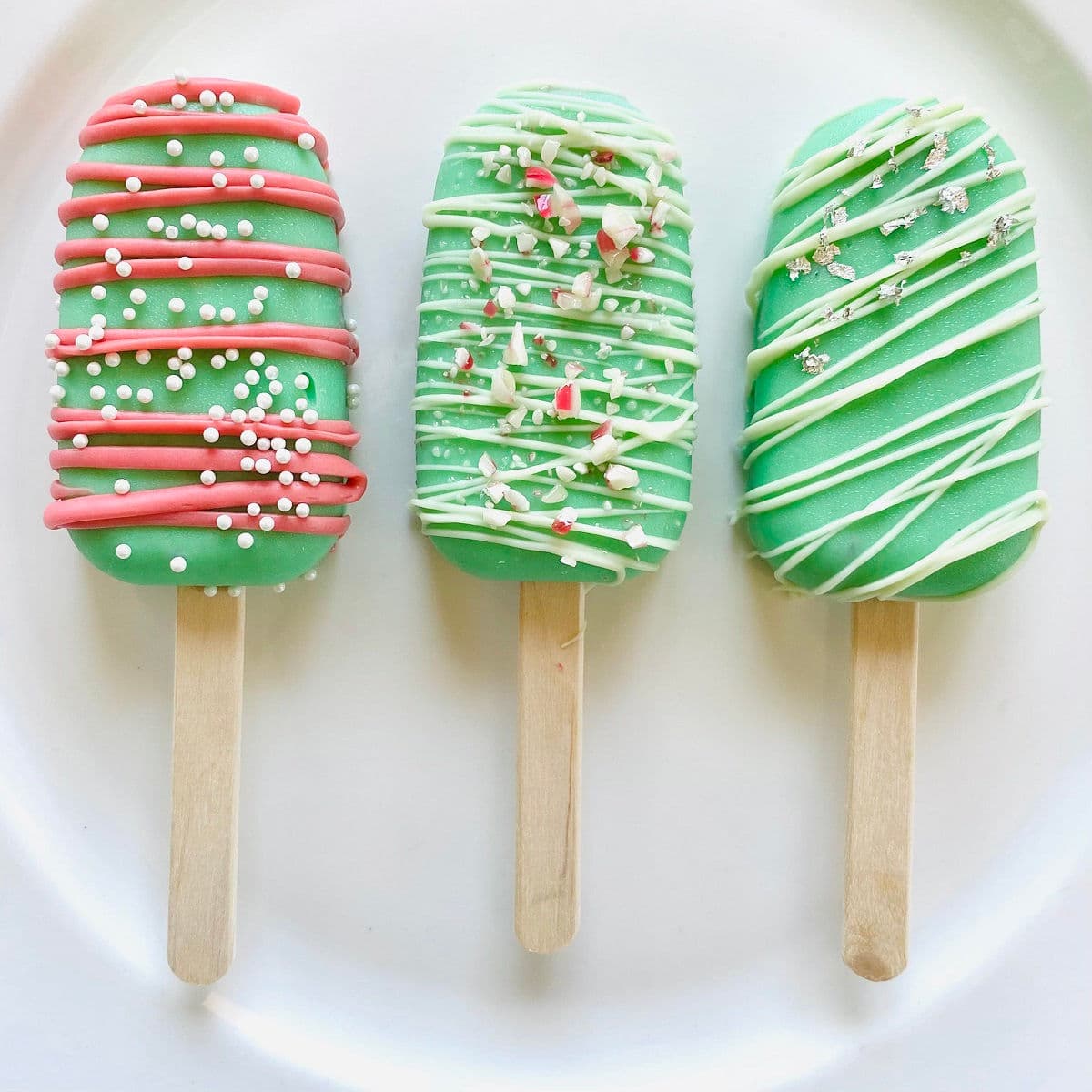 three Christmas cake popsicles on a plate in a row