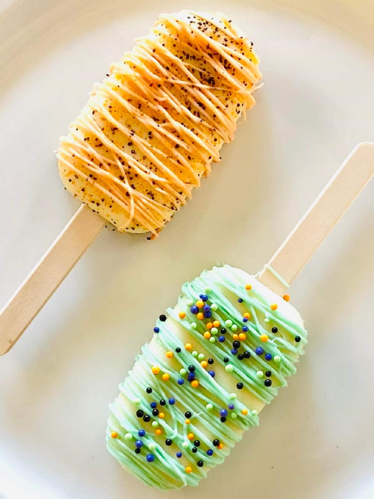 two halloween cakesicles on a plate decorated with sprinkles