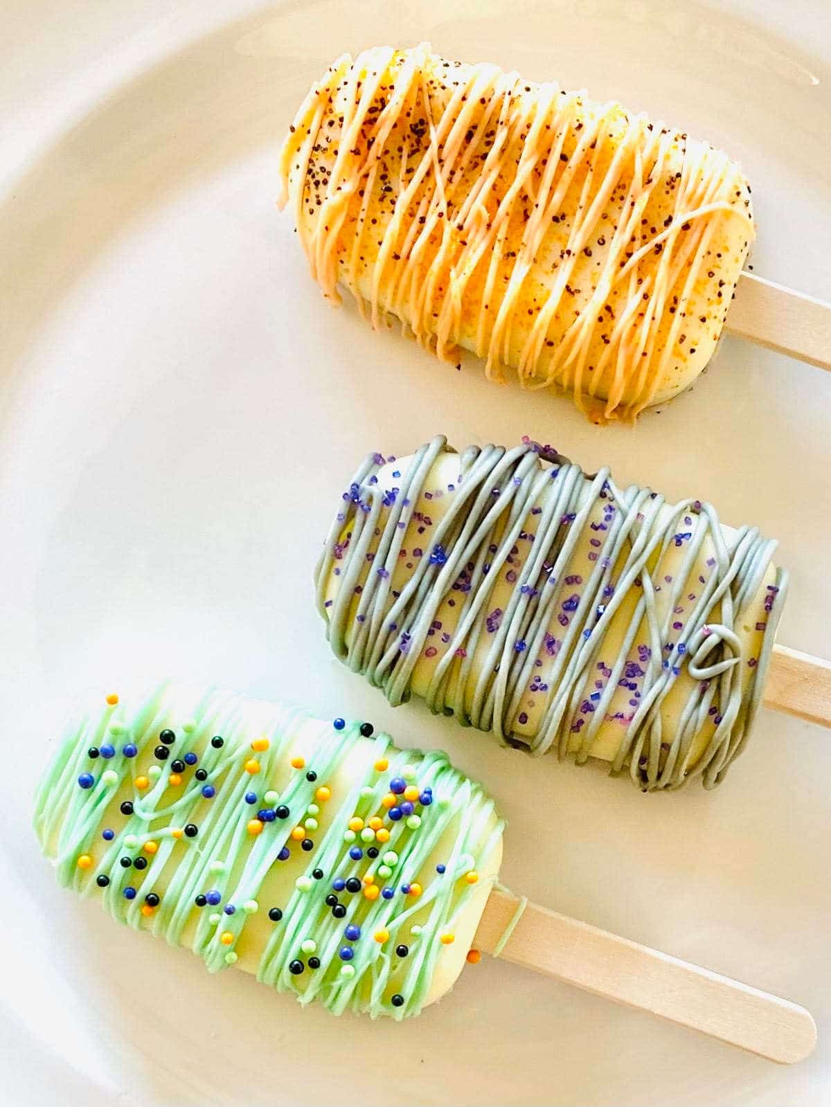 Three halloween cake popsicles on a plate decorated with sprinkles.