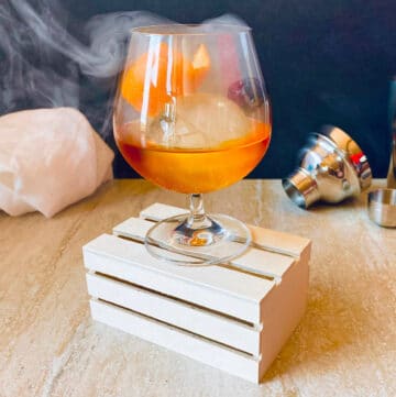 classic old fashioned in a glass with smoke garnished with orange and cherry