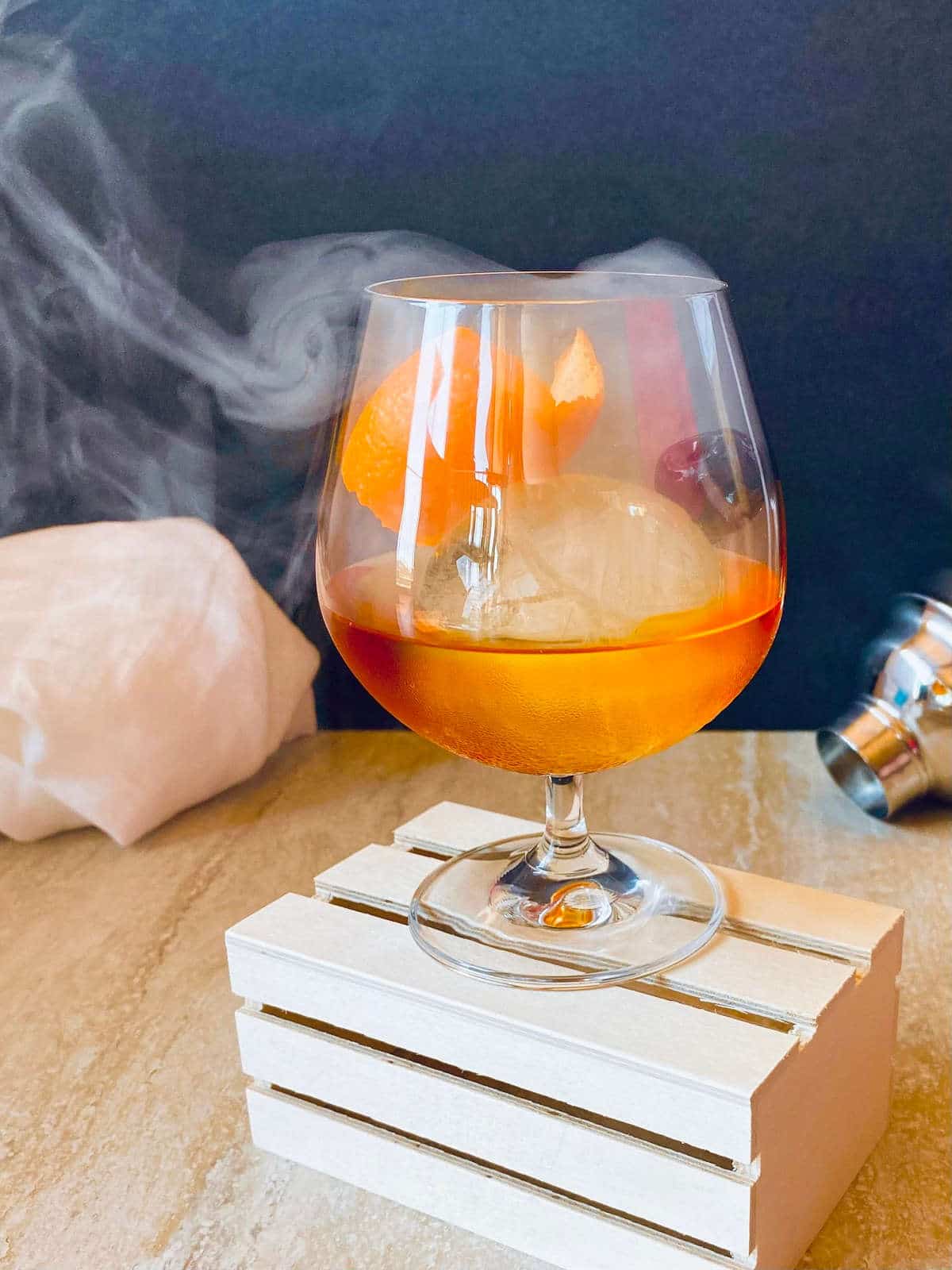 classic old fashioned in a glass with smoke garnished with orange and cherry