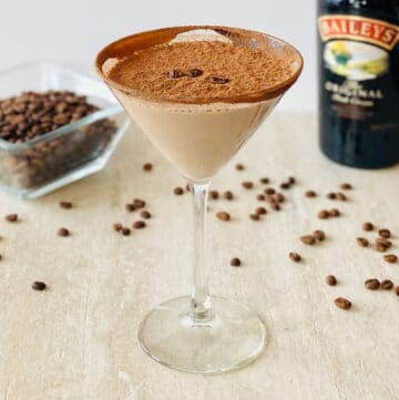 creamy espresso martini in martini glass with baileys and espresso beans in the background