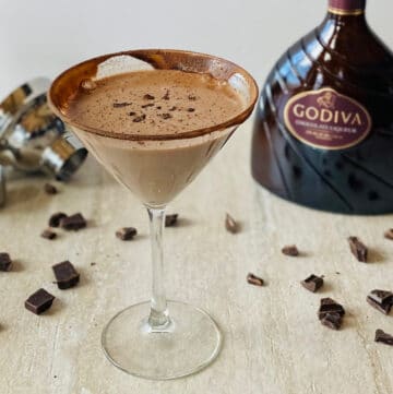 godiva chocolate liqueur drinks in a martini glass with a bottle of Godiva chocolate liqueur, a cocktail shaker and chocolate in the background