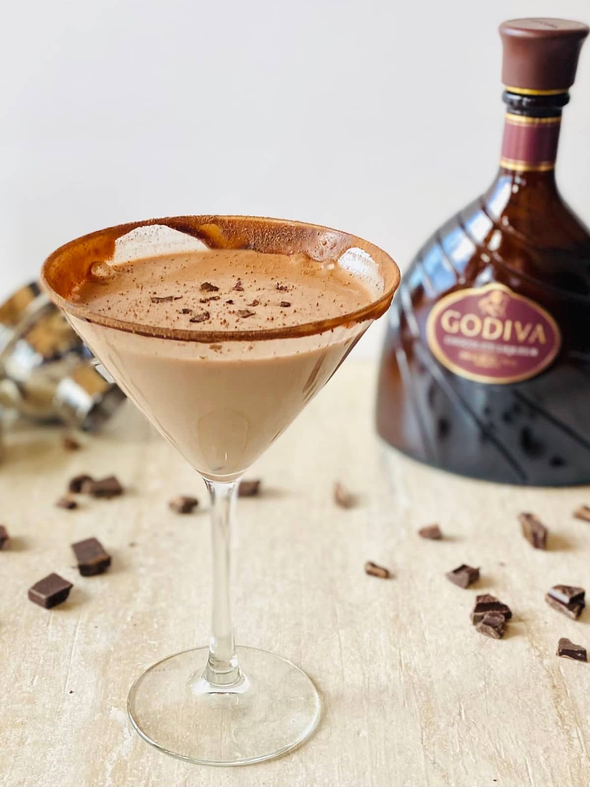 godiva chocolate liqueur martini in a martini glass with a bottle of Godiva chocolate liqueur, a cocktail shaker and chocolate in the background