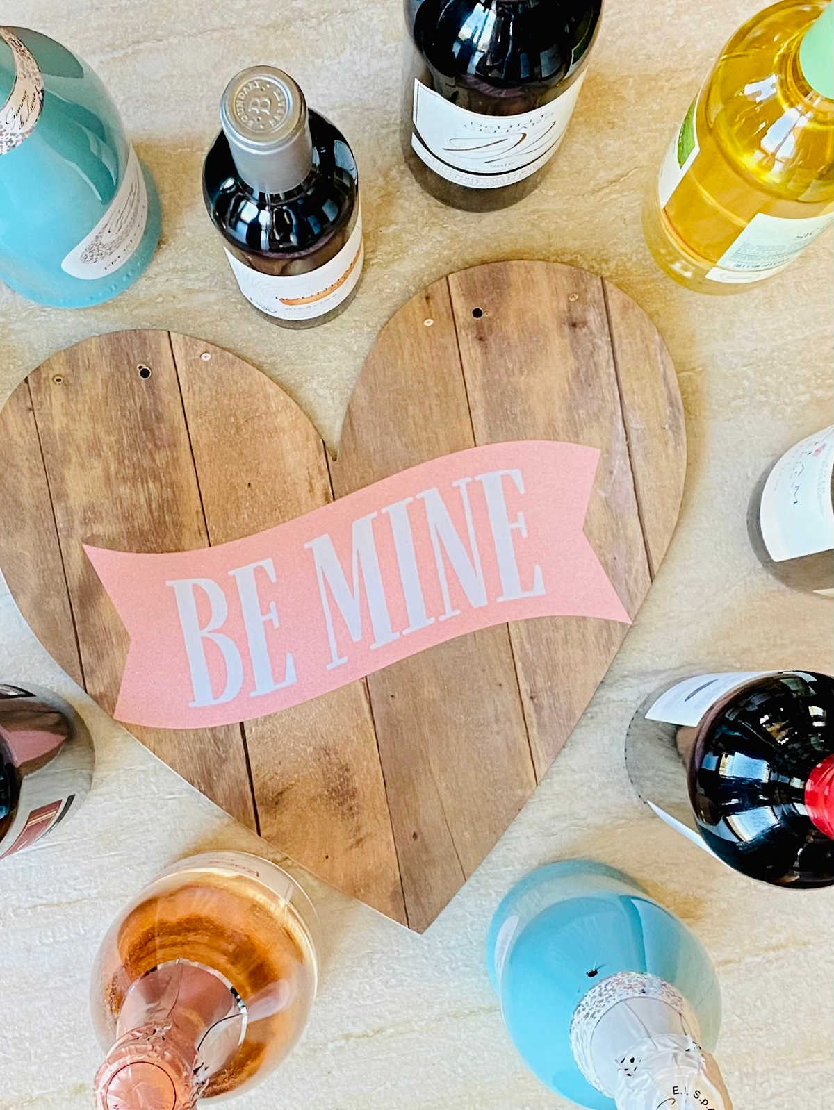 a heart board that says "be mine" surrounded by different bottles of wine