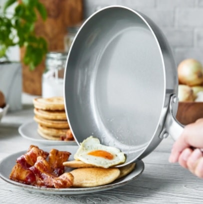 pan sliding egg on to a plate with bacon and pancakes