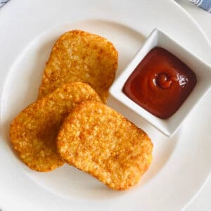 air fryer hash brown patties on a plate with ketchup