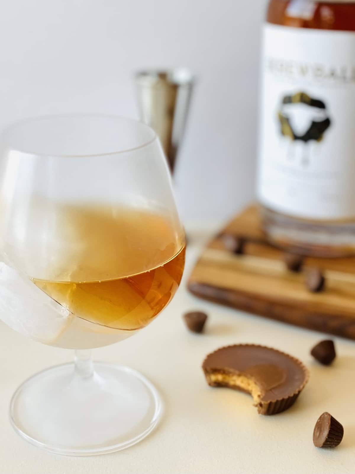peanut butter whiskey in a brandy snifter with ice and a peanut butter cup on the side