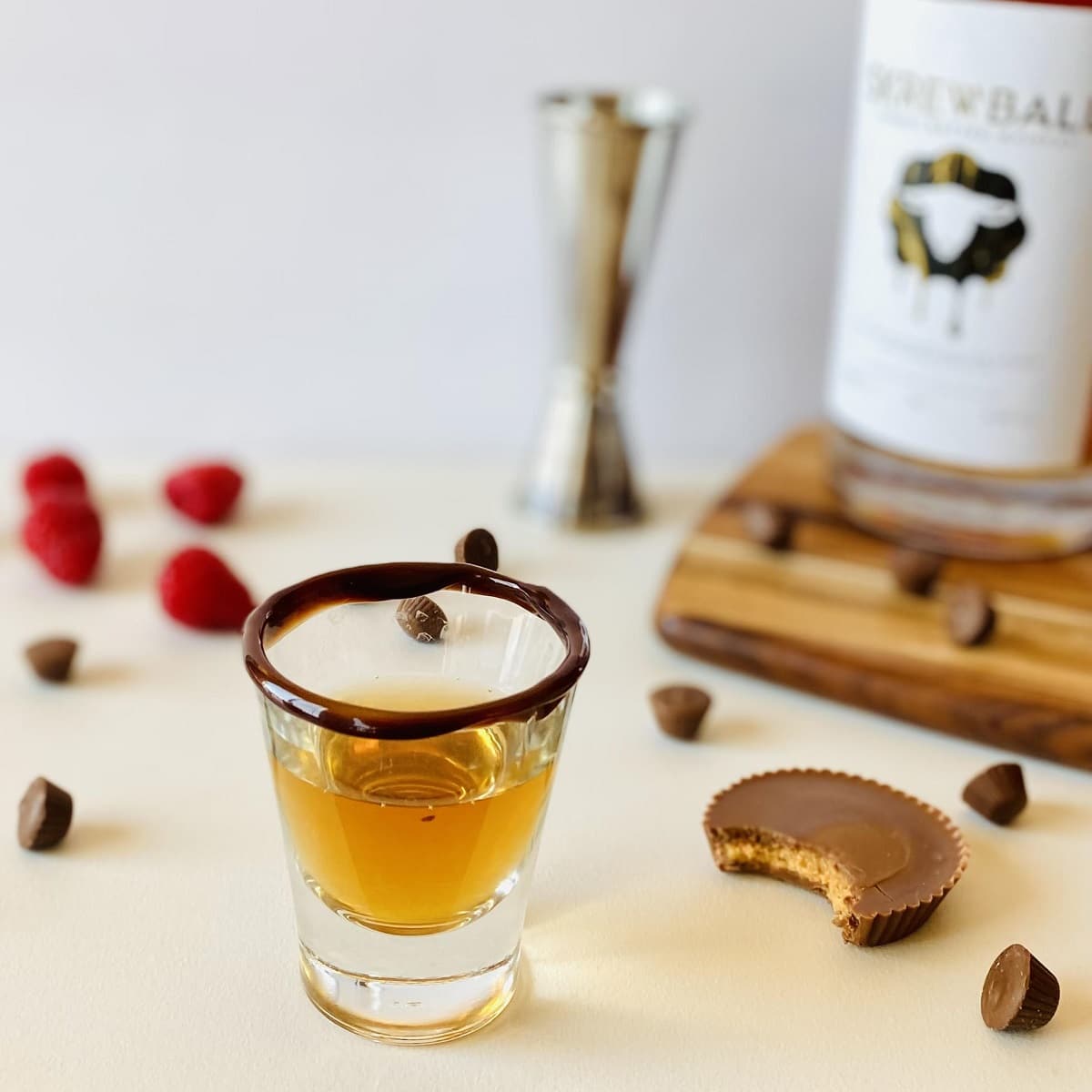 peanut butter whiskey cocktail in a shot glass with a chocolate rim next to a peanut butter cup with a bite out of it