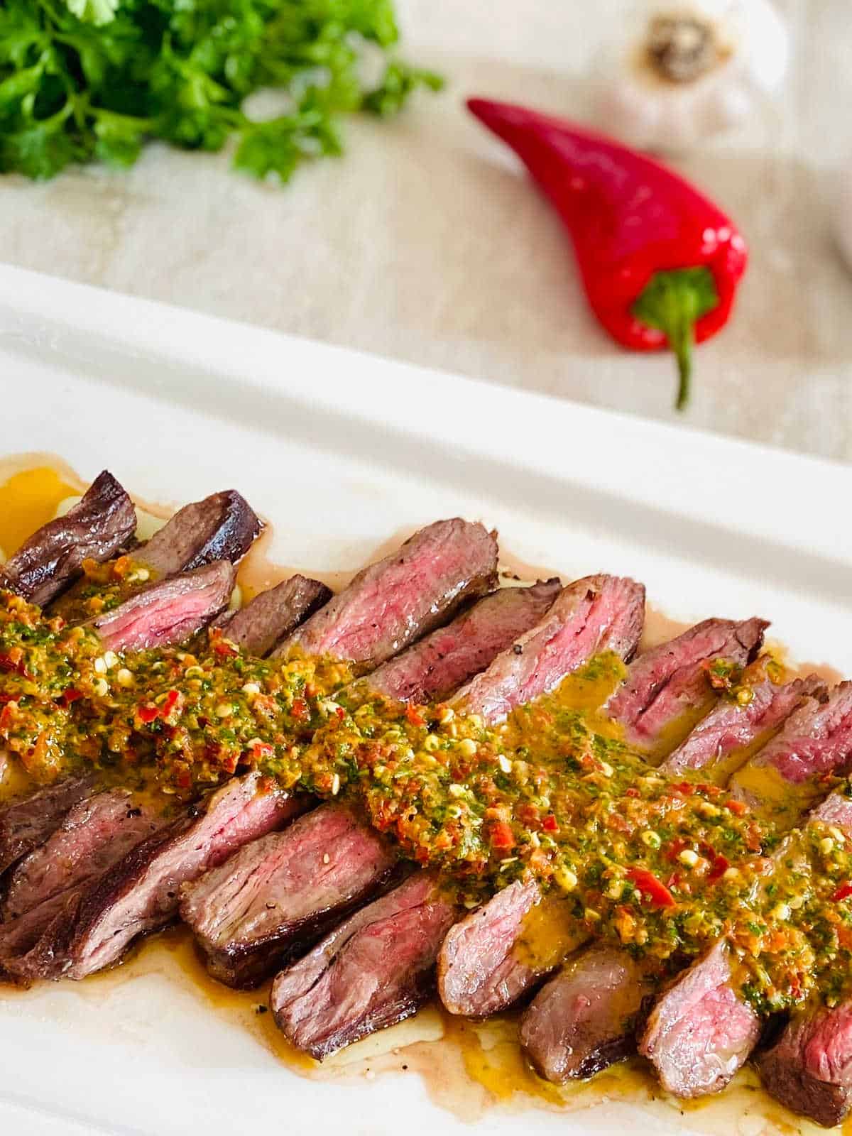 denver steak sliced with red pepper and garlic in background