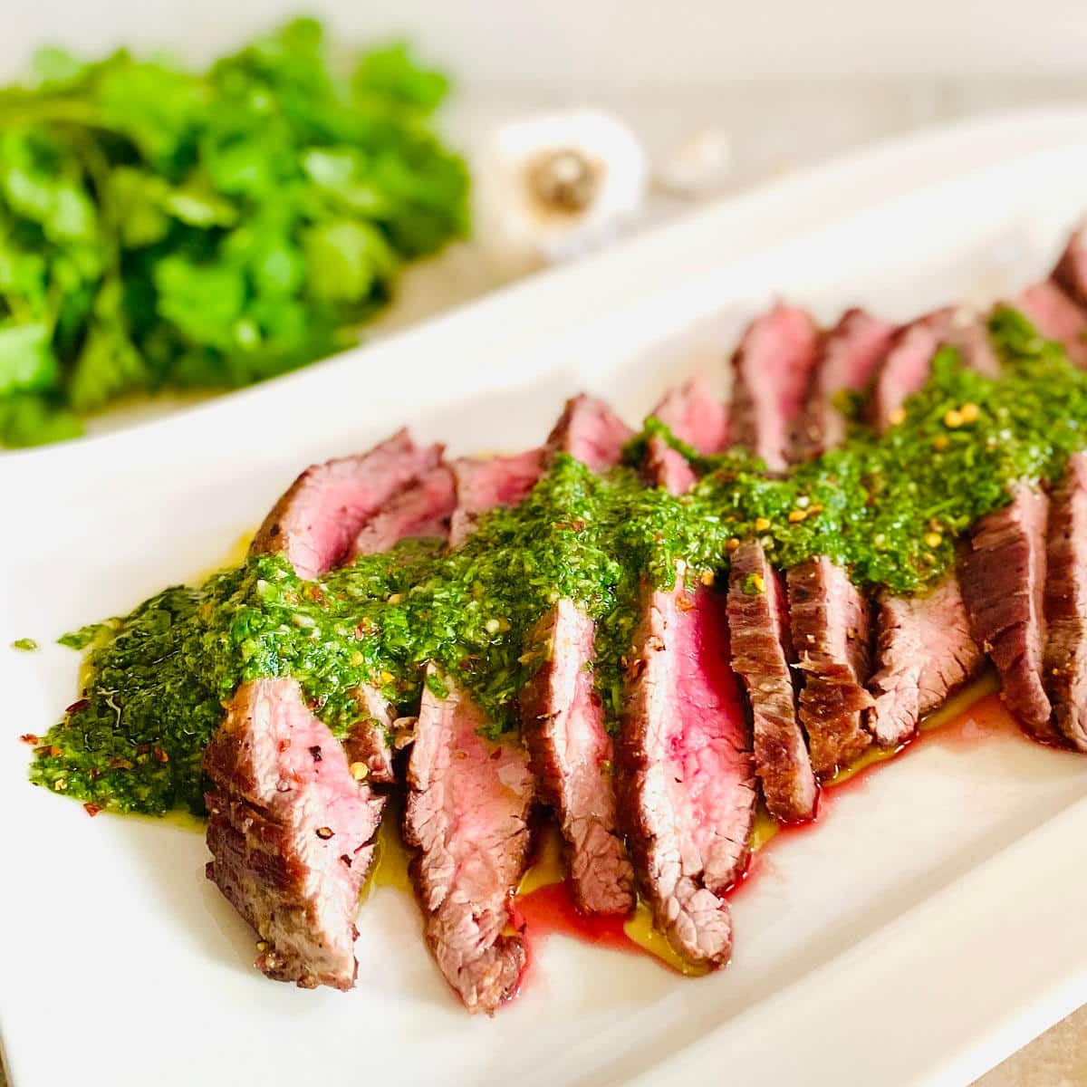 spicy chimichurri sauce over sliced steak with fresh cilantro and garlic in the background