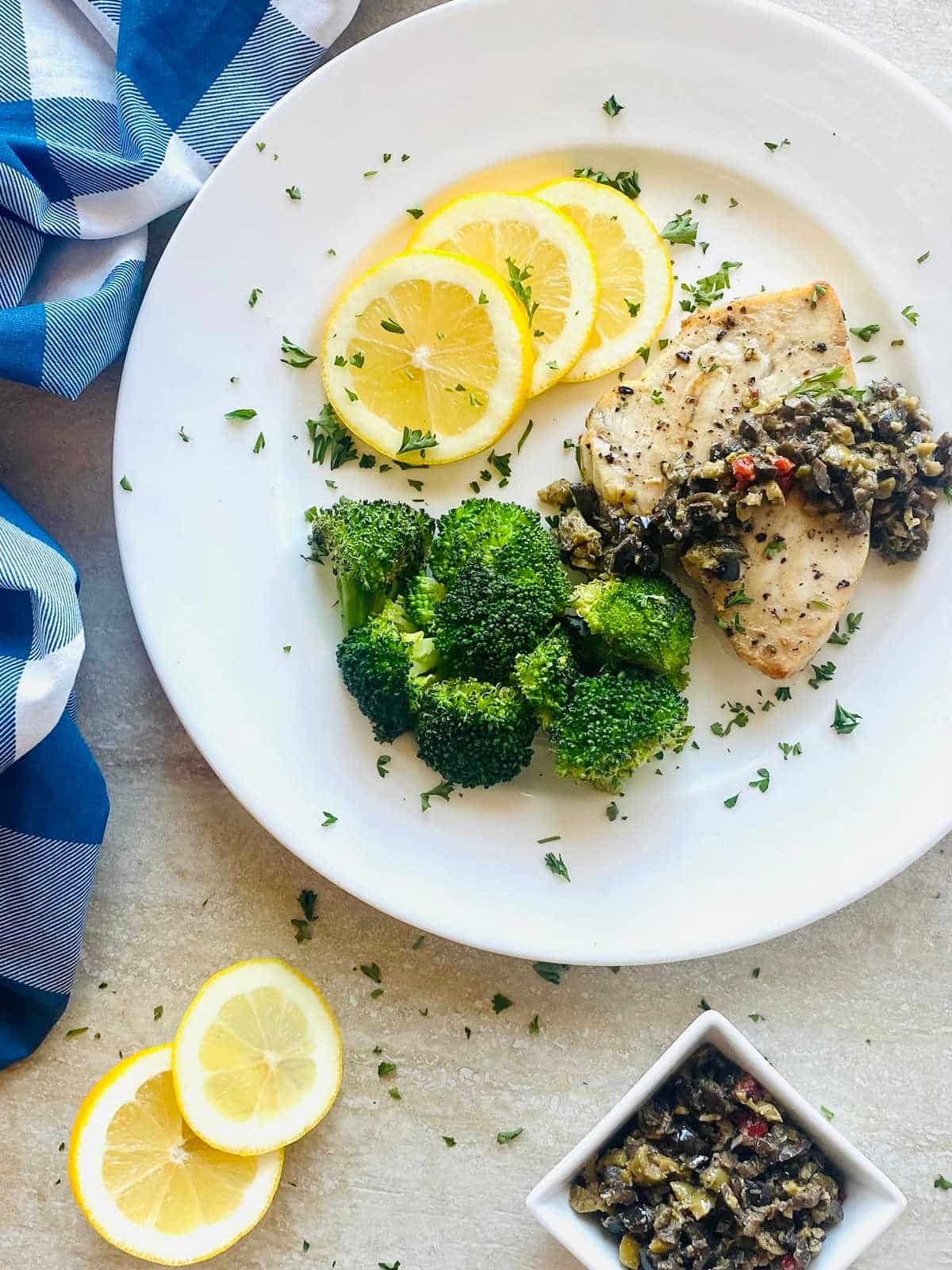 air fryer swordfish on a plate with lemon slices, broccoli and topped with olive tapenade