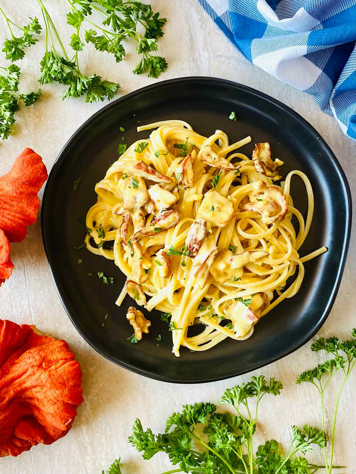 lobster mushroom pasta recipe on a black plate next to fresh lobster mushrooms, parsley and a blue napkin