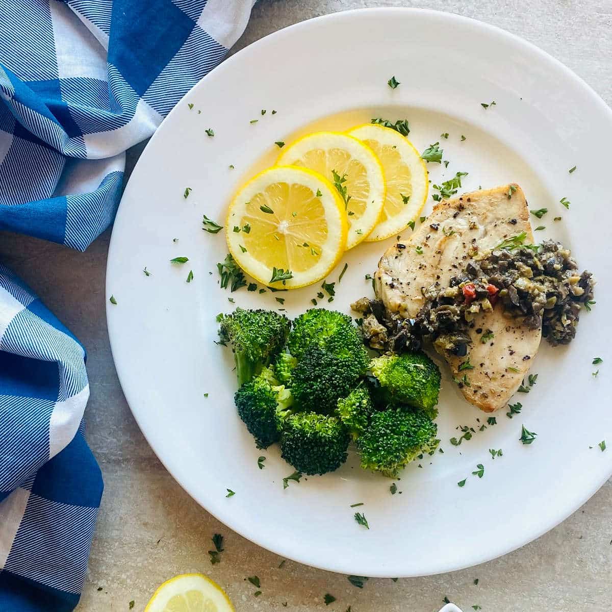 swordfish air fryer on plate with olive tapenade, lemon slices and broccoli