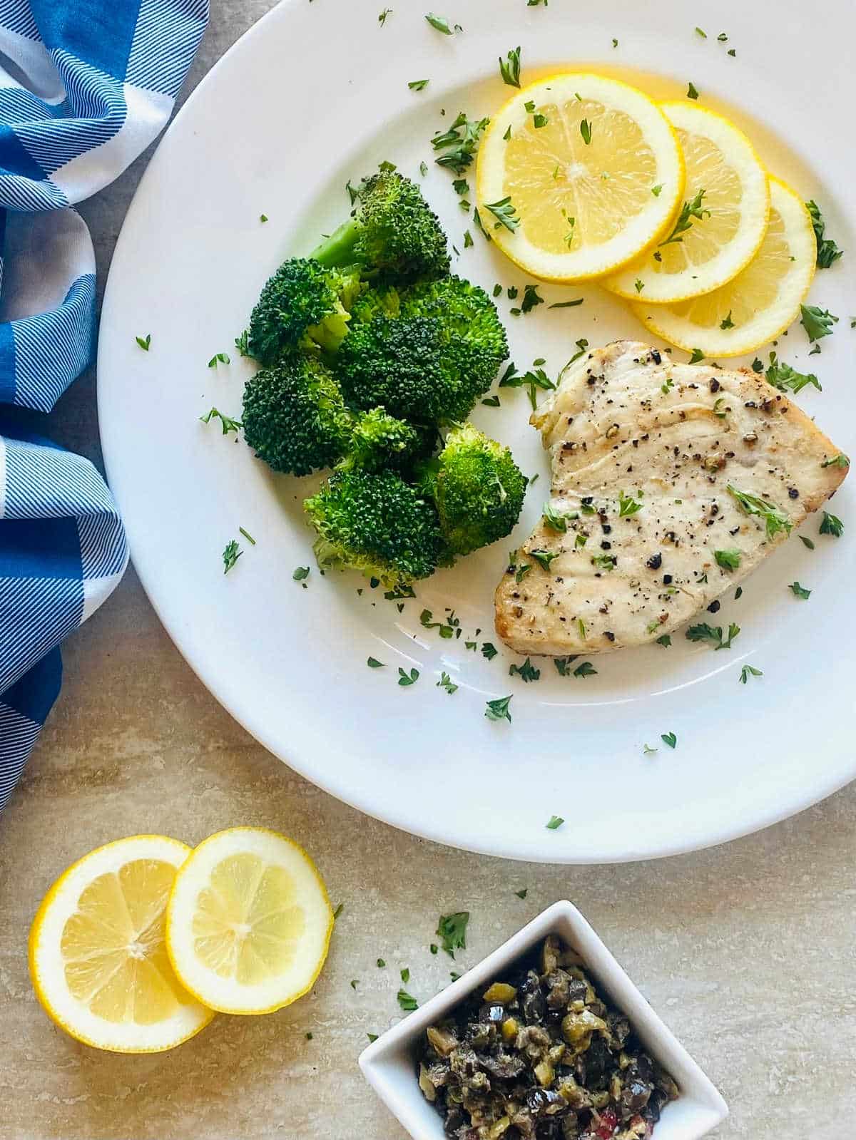swordfish cooked in air fryer on a plate with lemon sliced and broccoli