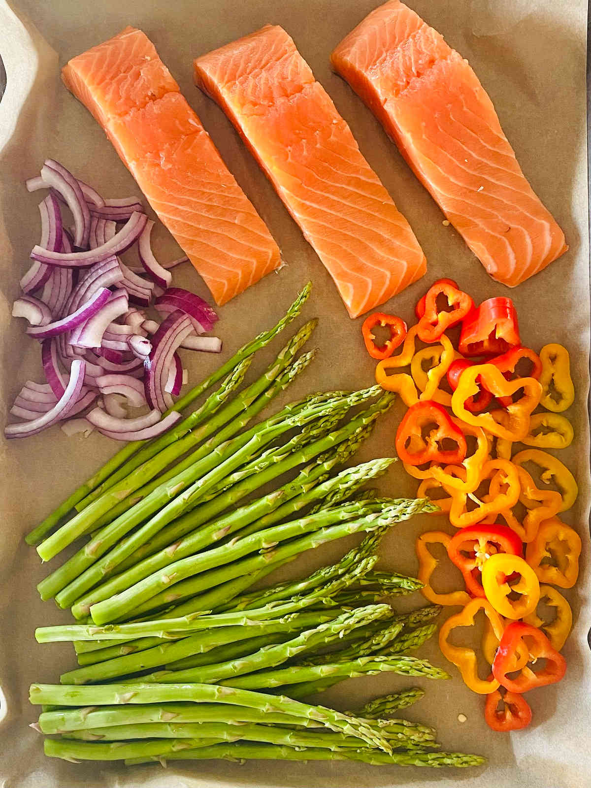 raw salmon, sliced peppers, sliced onions and asparagus on a sheet pan before cooking.
