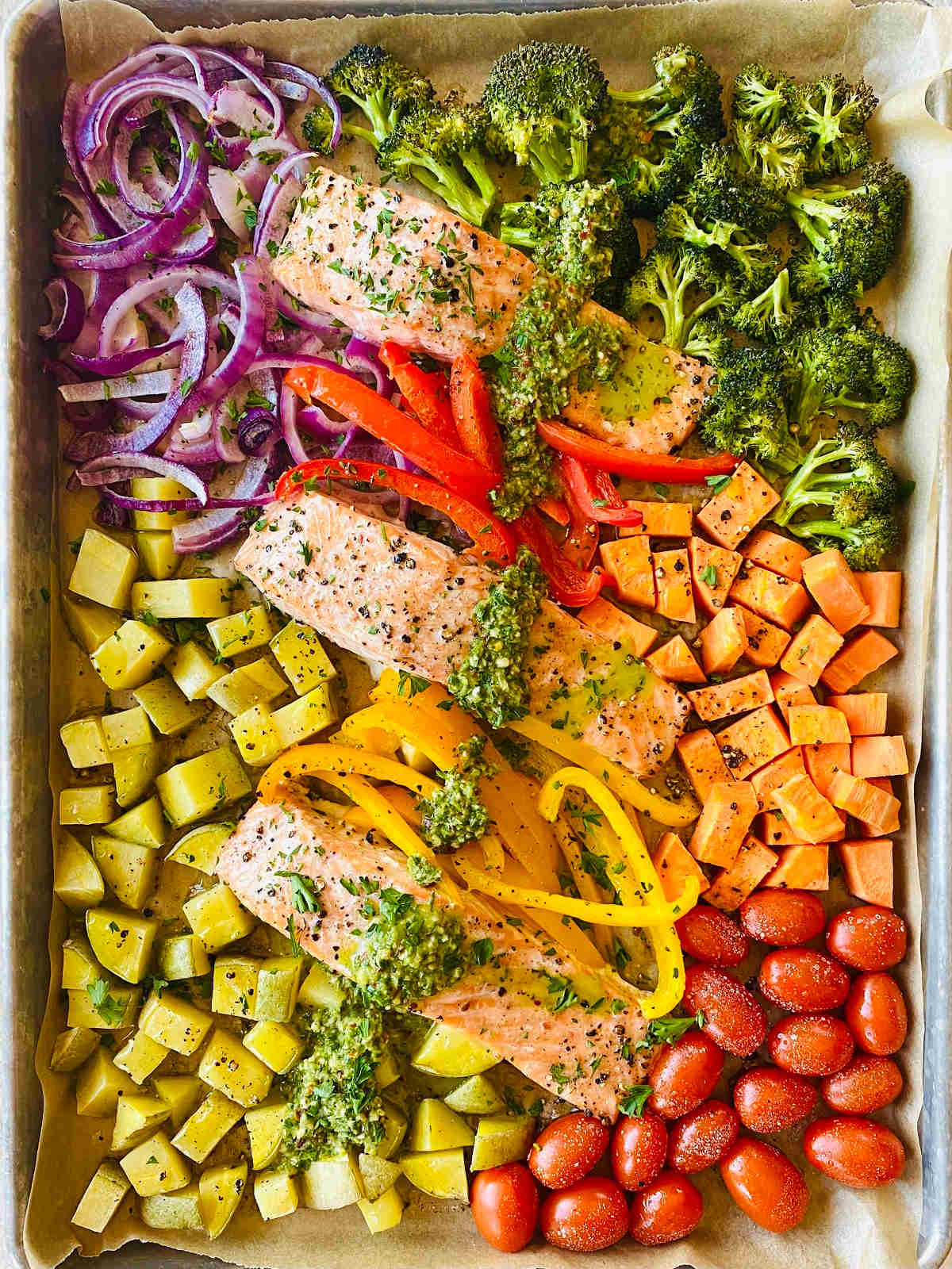 sheet pan salmon with broccoli, onion, potato, sweet potato, peppers and tomatoes with a drizzle of chimichurri sauce.