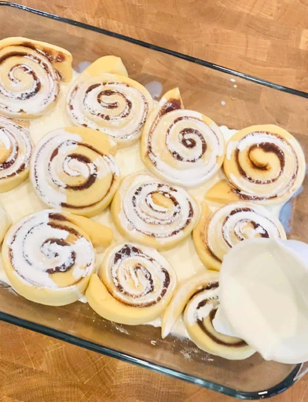 rhodes cinnamon rolls with heavy cream being poured on top.