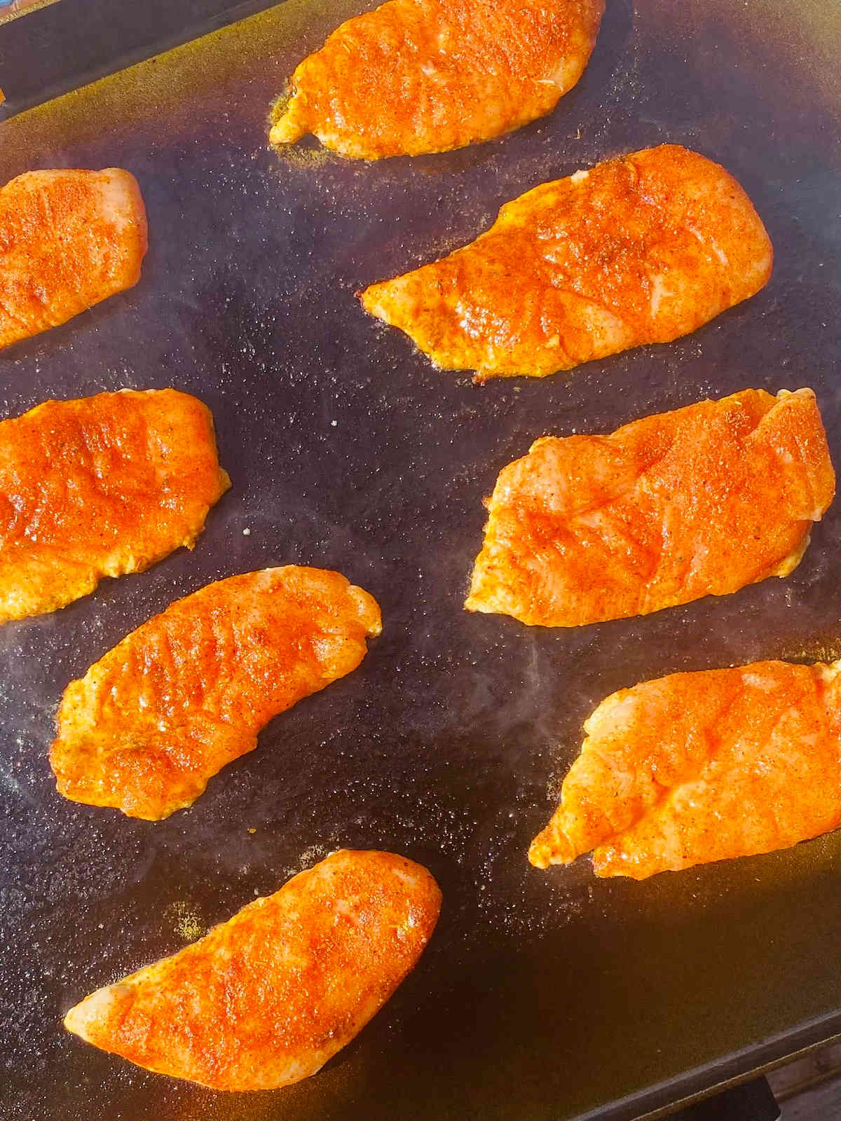 how to season a flat top grill process shot with chicken cooking on blackstone griddle.