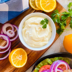 mayonnaise recipe in bowl next to lemons and a sandwich.