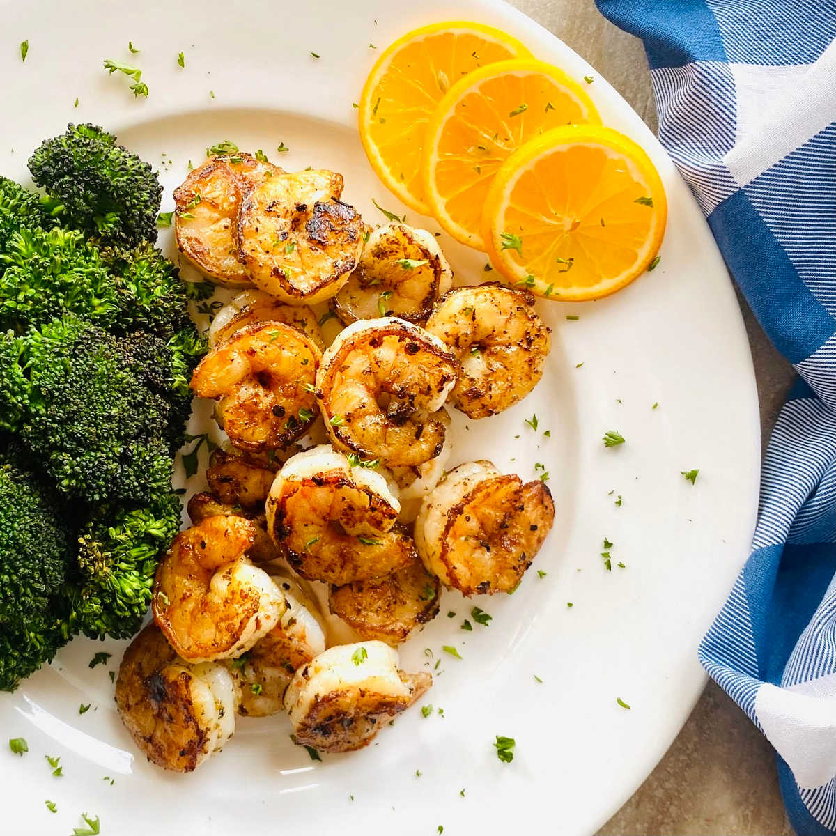 pan seared prawns on a plate with lemon, broccoli and garnished with parsley.