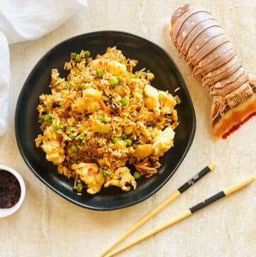 lobster fried rice recipe on plate with chili oil, chopsticks and lobster tail.