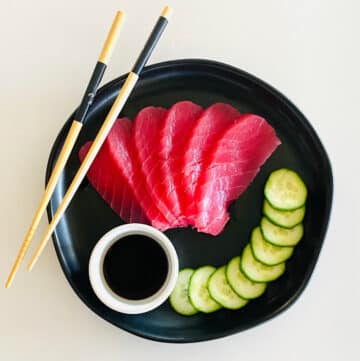 tuna sashimi recipe fully prepared on plate with soy sauce, sliced cucumbers and chopsticks.